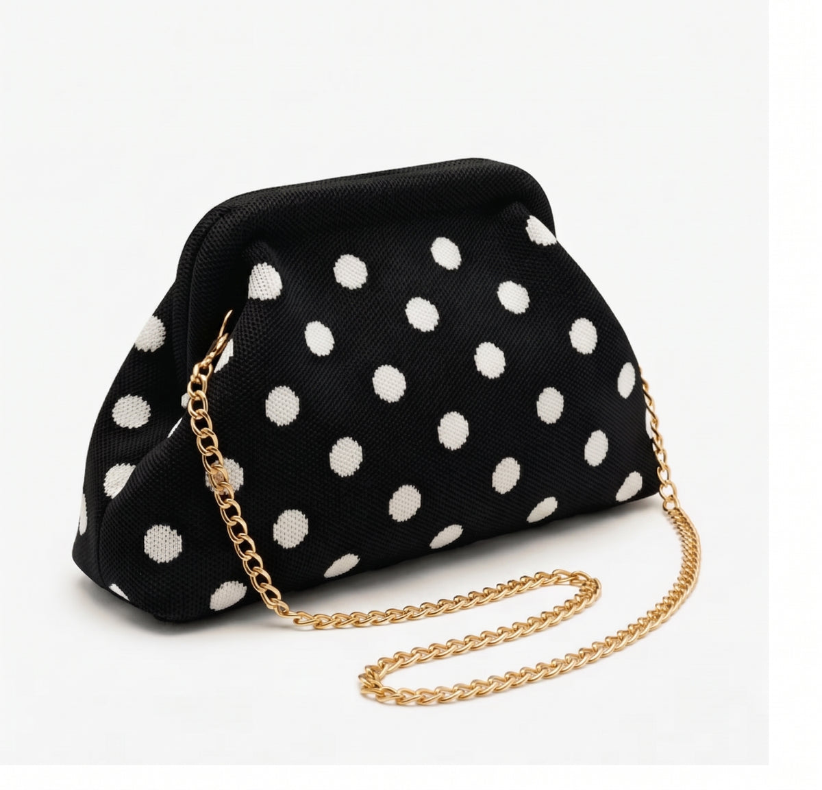 Bolso bandolera de mano modelo Noa en color negro con estampado de lunares blancos, cierre metálico de boquilla y cadena dorada de SEVALA sobre fondo blanco.