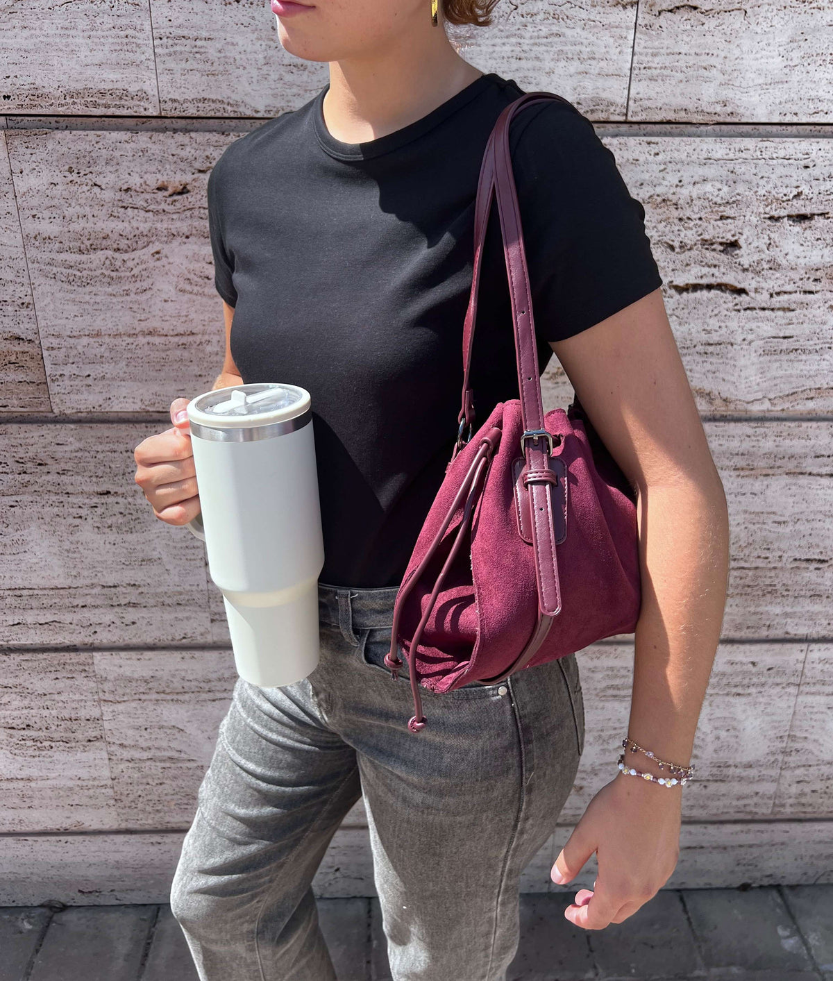 Mujer con camiseta negra y gafas de sol llevando el bolso POD burdeos colgado al hombro en la calle, mostrando la caída natural del bolso y su tamaño real para el día a día