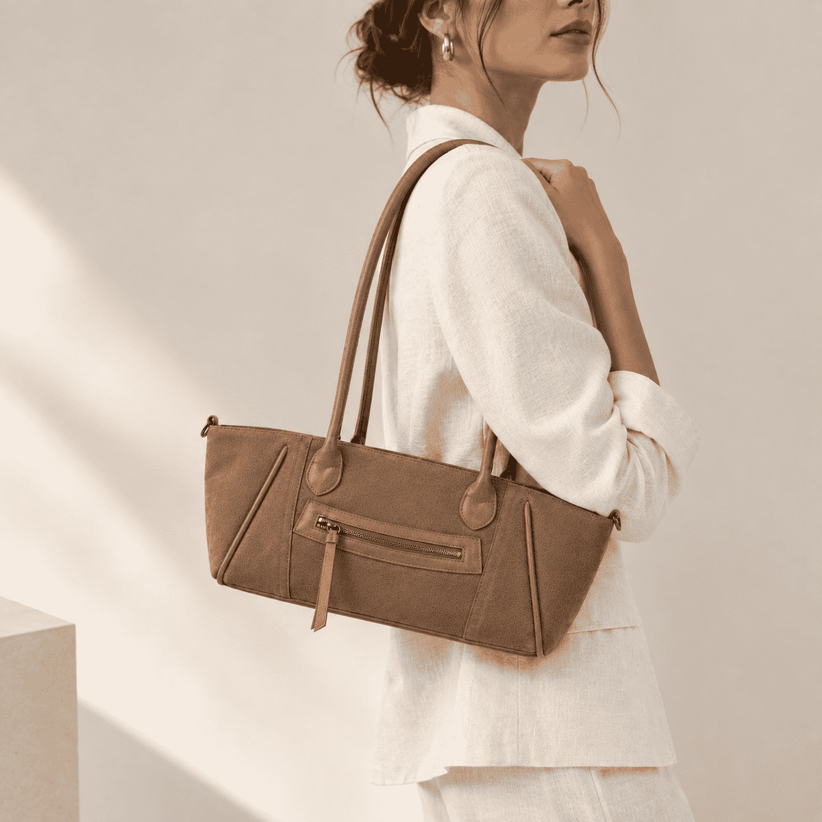 Bolso de hombro Terra Camel para mujer, modelo alargado tipo baguette, llevado por una modelo de perfil. El bolso presenta una textura grabada y un bolsillo exterior con cremallera.