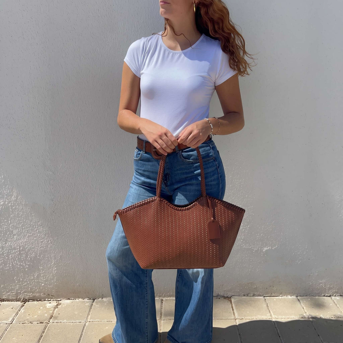 Modelo sosteniendo el bolso tote marrón con diseño de piel trenzada sobre fondo claro.