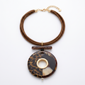 Collar corto de SEVALA con cordón marrón en capas, detalles metálicos dorados y colgante circular grande con estampado carey y animal print sobre fondo blanco.