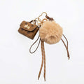 Texto alternativo (Alt Text):
Llavero y charm para bolso con mini bolso marrón estampado, pompón de pelo sintético beige, cordones marrones y detalles dorados sobre fondo blanco.